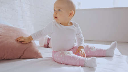 surprised adorable toddler child sitting on bed near pink pillowの写真素材