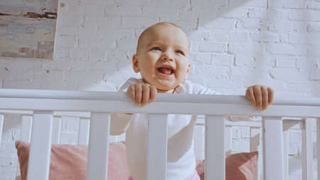 low angle view of excited baby girl standing in white baby crib at homeの写真素材