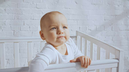 adorable baby with blue eyes standing in white baby crib at homeの写真素材