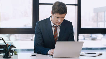 businessman in suit typing on laptop near notebook and mobile phone