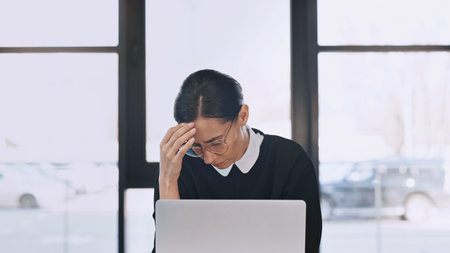 exhausted businesswoman in eyeglasses touching forehead while suffering from headache near laptopの写真素材