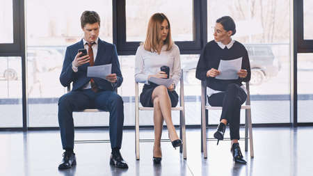 woman with coffee to go sitting near job seekers with resumes in office