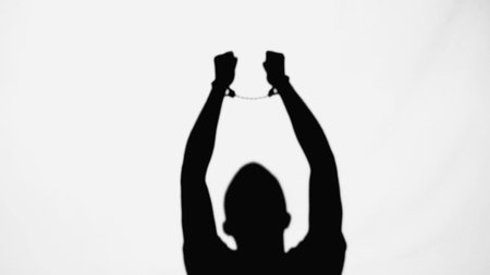 silhouette of criminal man with handcuffs on raised hands isolated on whiteの写真素材