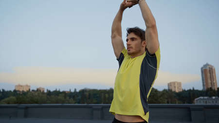 Young sportsman stretching on roof in evening