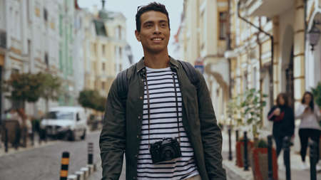 Smiling bi-racial tourist with film camera walking on urban european streetの写真素材