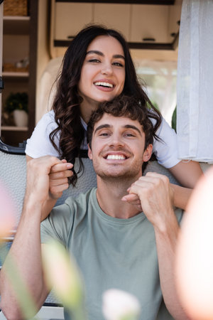 Happy young couple holding hands and smiling at camera near camper vanの写真素材
