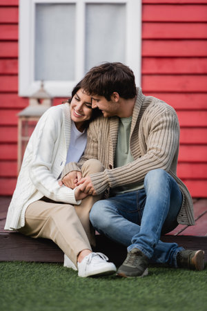 Smiling couple in warm cardigans holding hands on terrace of houseの写真素材