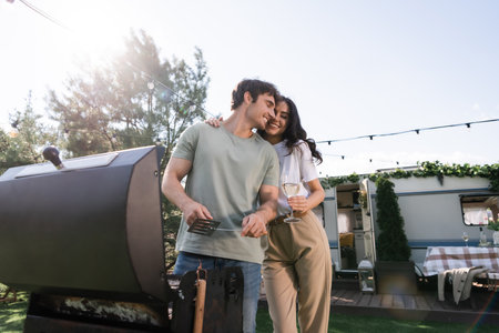 Low angle view of smiling couple holding wine and cooking near camper vanの写真素材