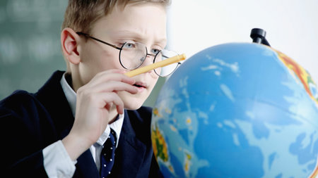 schoolboy in glasses pointing with pencil at globe in classroomの写真素材