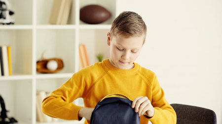 schoolboy in yellow jumper holding backpack at home