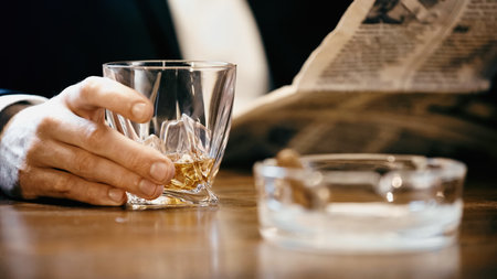 Cropped view of businessman holding glass of whiskey and newspaper near ashtray isolated on blackの写真素材