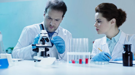 scientist holding glass with sample near colleague in white coat holding pencil in lab