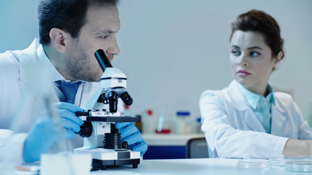 scientist making analysis with microscope near pretty colleague sitting in laboratoryの写真素材