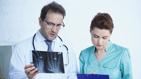 radiologist holding x-ray while nurse writing on clipboard in clinic