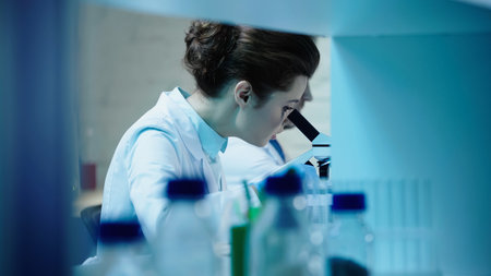 scientist looking in microscope near blurred colleague in laboratory