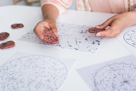 partial view of young astrologer holding clay runes near cosmic maps at homeの写真素材