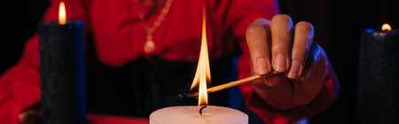 partial view of fortune teller lighting palo santo stick near burning candle isolated on black,...