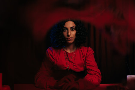 young fortune teller looking at camera on dark background with red smoke