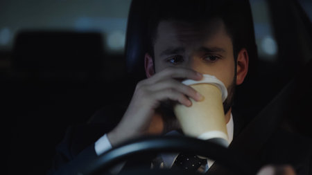 businessman driving car at night and drinking coffee to goの写真素材