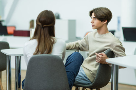 student looking at blurred teen girl while sitting in reading roomの写真素材
