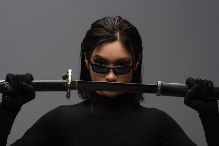 front view of asian woman in black outfit and stylish sunglasses pulling out katana from scabbard...