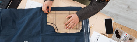 Top view of african american designer holding sewing print near cloth and smartphone, banner