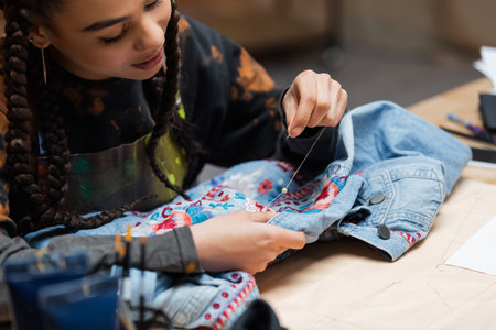 African american designer decorating denim jacket with embroidery in workshop