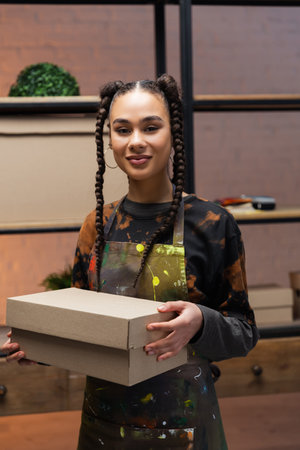 Smiling african american designer holding carton box in workshop