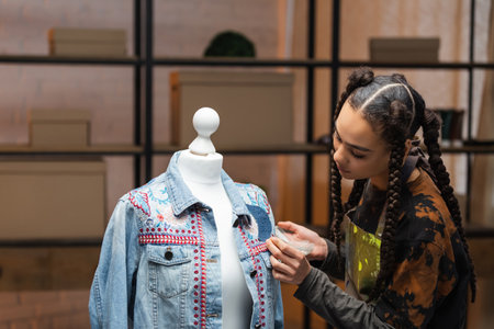 African american designer decorating denim jacket in workshop