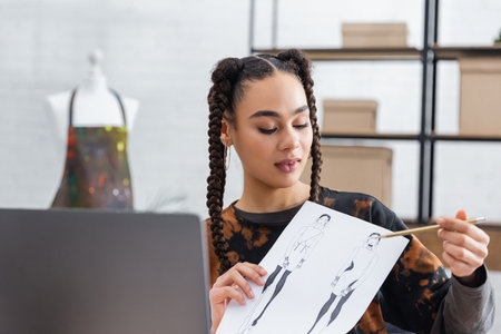 African american craftswoman pointing at sketch during video call on laptop