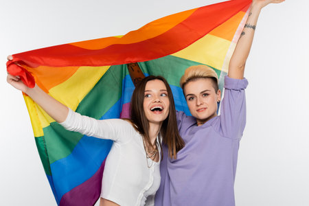 cheerful young lesbians holding lgbtq flag isolated on greyの写真素材