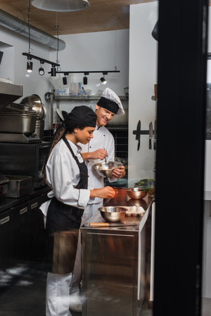 cheerful multiethnic chefs cooking together in professional kitchenの写真素材