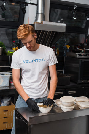 redhead volunteer covering bowl with plastic cup in kitchenの写真素材