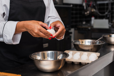 partial view of african american chef holding raw egg above bowl while cooking in kitchen