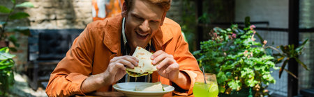 cheerful redhead man eating quesadilla near glass with cocktail in outdoor terrace, banner