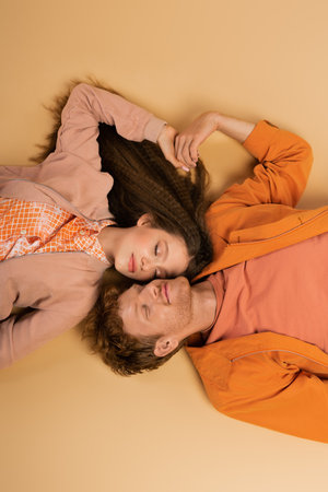 top view of pleased and young redhead man lying together with pretty girlfriend on beigeの写真素材