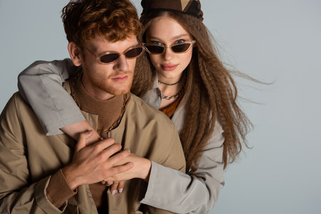 teenage girl in sunglasses hugging stylish and redhead boyfriend isolated on greyの写真素材