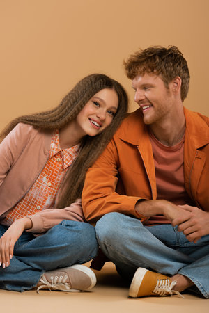 cheerful girl leaning on shoulder of happy boyfriend isolated on beigeの写真素材