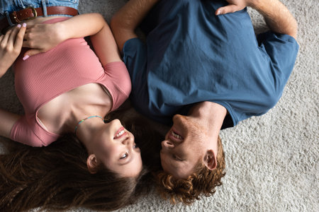 top view of cheerful young couple smiling and lying together on carpet in living room