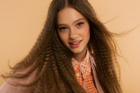 cheerful teenage girl looking at camera while posing isolated on beige