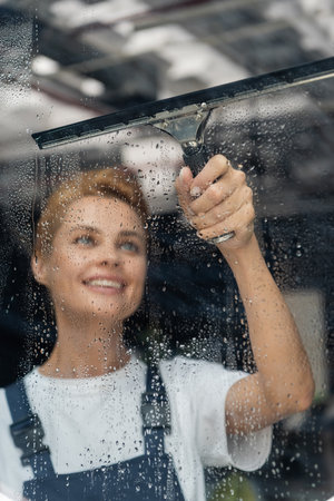 professional cleaner with window squeegee smiling near wet glass in officeの写真素材