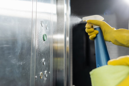 partial view of man spraying detergent while cleaning elevator