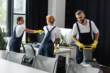 young bi-racial woman wiping computer monitor near colleagues cleaning officeの写真素材