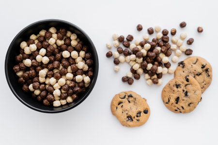 top view of cereal balls in bowl near chocolate chip cookies isolated on whiteの写真素材