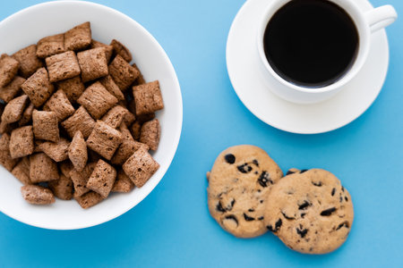 top view of cereal puffs in white bowl near cup of coffee and chocolate chip cookies isolated on blueの写真素材