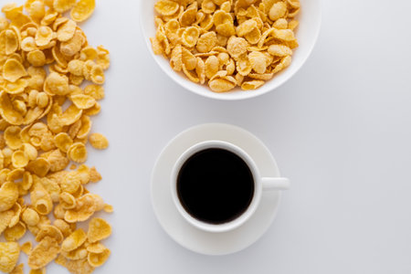 top view of bowl with corn flakes near cup of black coffee isolated on white