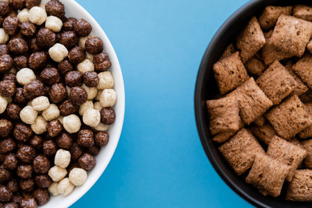 top view of bowls with tasty cereal balls and puffs isolated on blueの写真素材