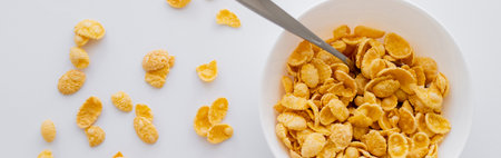 top view of bowl with crispy corn flakes and spoon isolated on white, banner