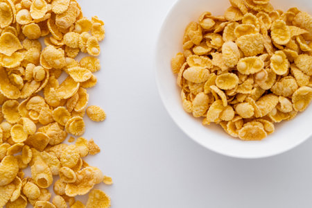 top view of dry and crispy corn flakes near bowl isolated on white