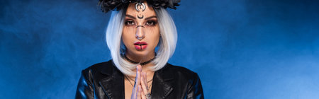 young woman in witch halloween makeup with praying hands on blue foggy background, banner